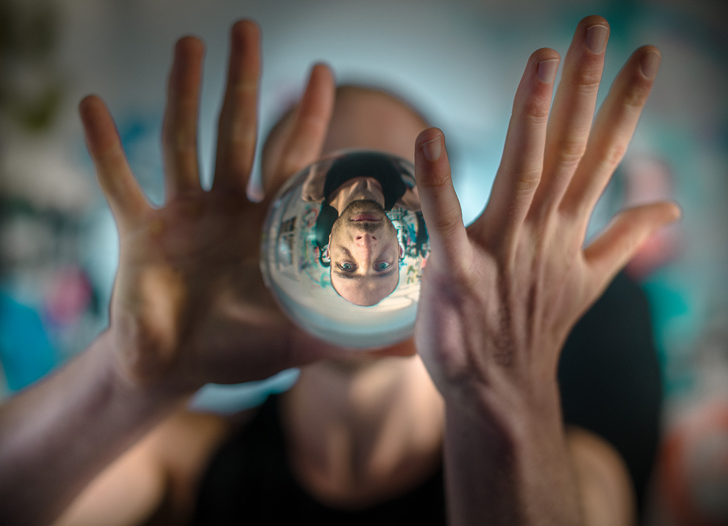 Colour photographic portrait of male manipulating solid glass sphere his face seen thruogh the ball upside down.